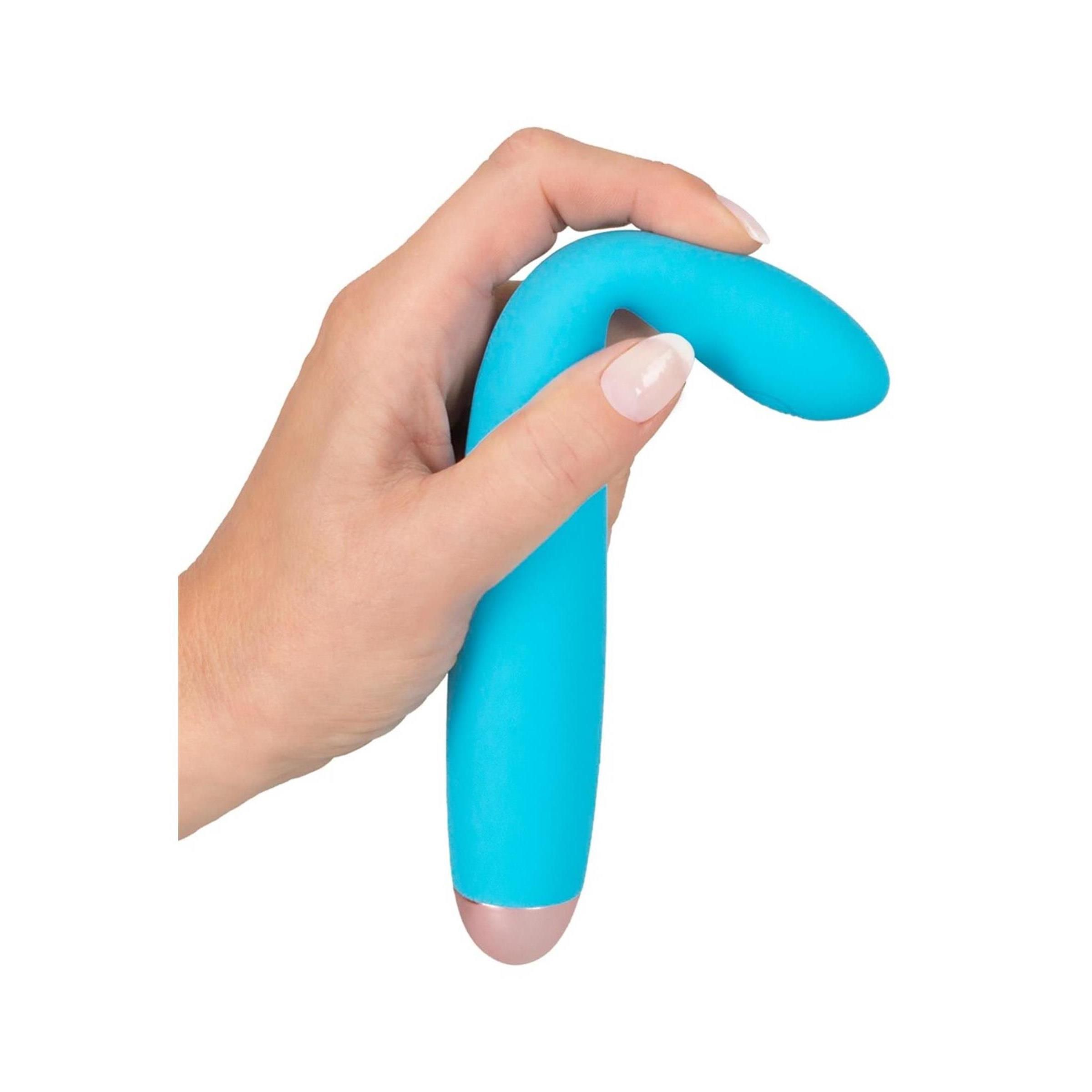 Hand hält türkisfarbenen Vibrator mit gebogener Form und goldfarbener Spitze. Auf weißem Hintergrund.