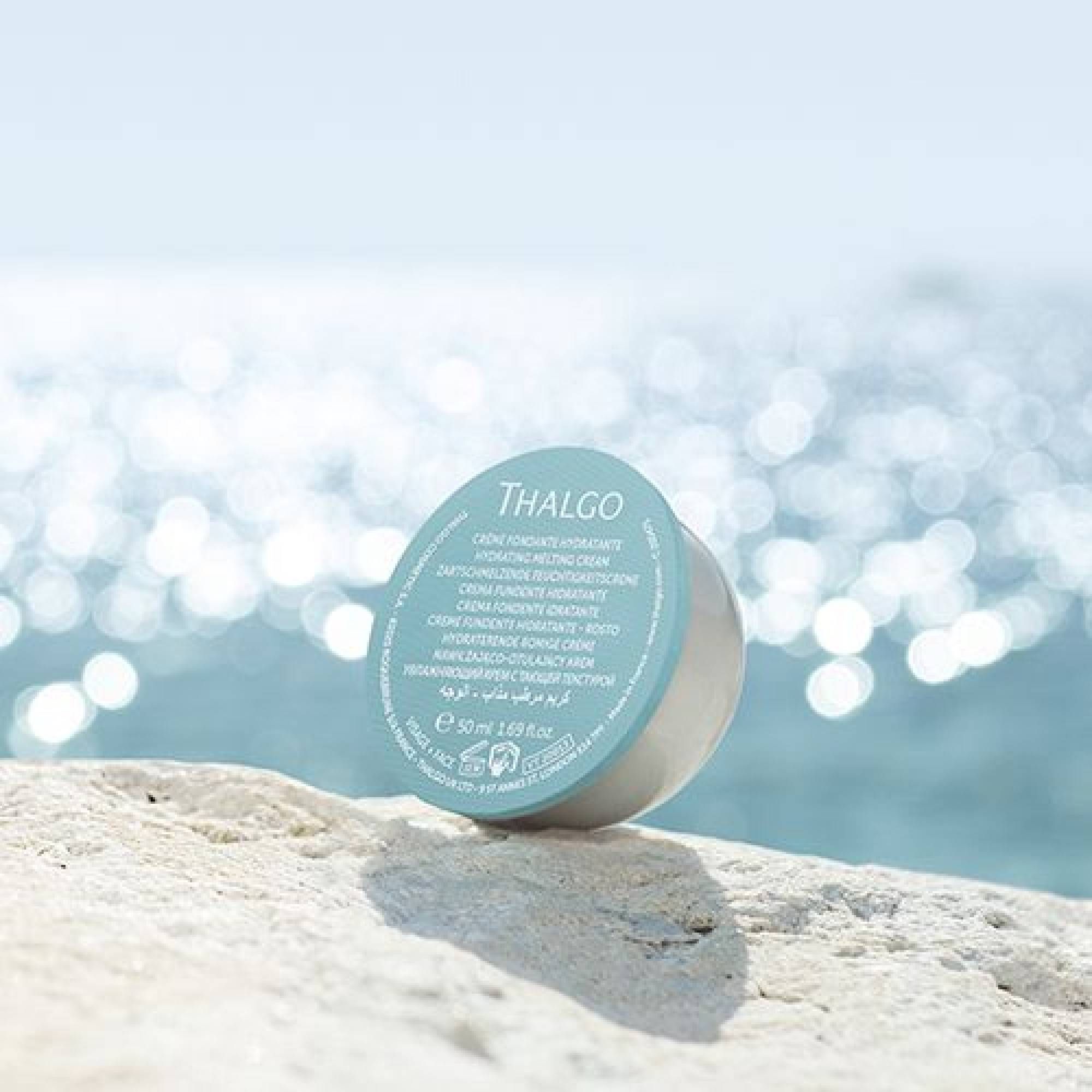 Creme-Verpackung auf Stein vor verschwommenem Meer. Blauer Deckel mit THALGO-Logo und Text. Mehrsprachiger Text. 50 ml.