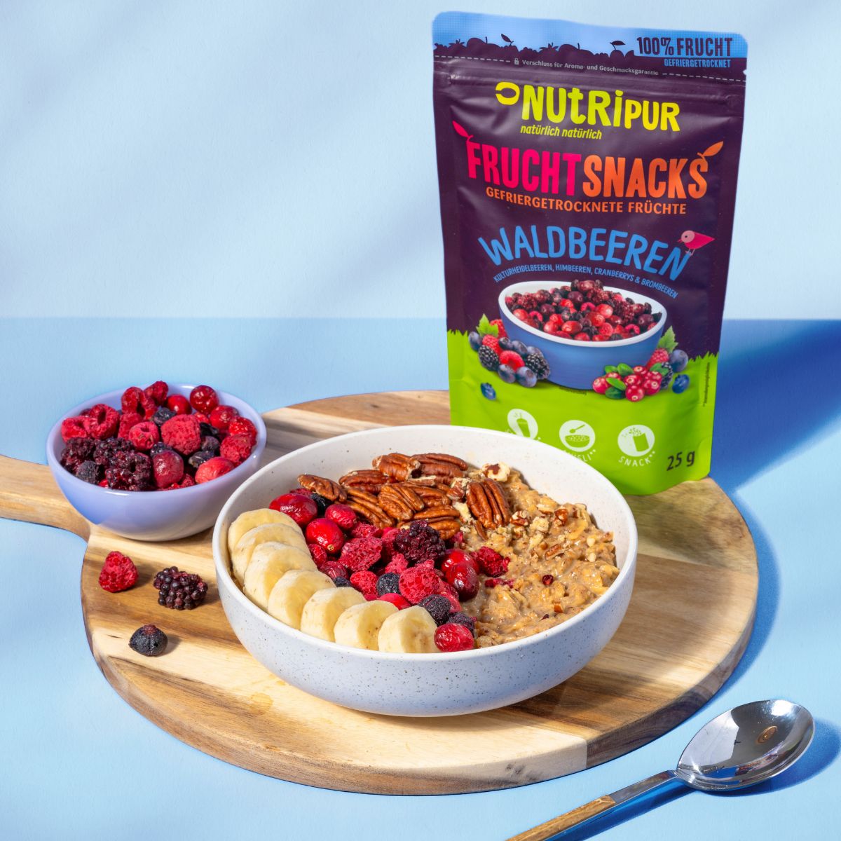 Frühstück mit Müsli, Bananenscheiben, Beeren und Pekannüssen. Daneben eine Packung NutriPur Waldbeeren und eine Schüssel mit Beeren.
