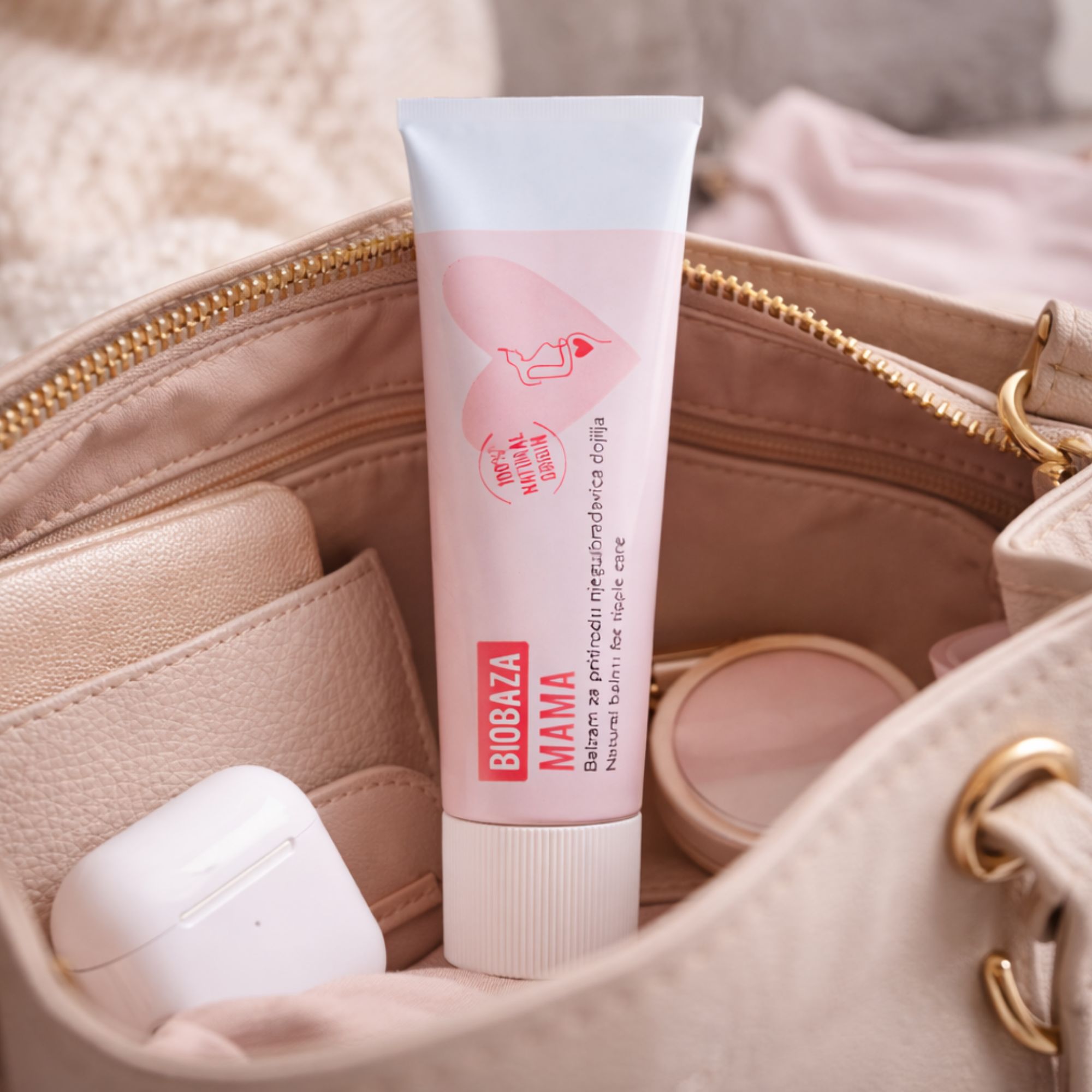 Rosa Tube in einer Handtasche. Aufgedruckt: Biobaza Mama, Balsam für Brustwarzen. Weitere Gegenstände in der Tasche.