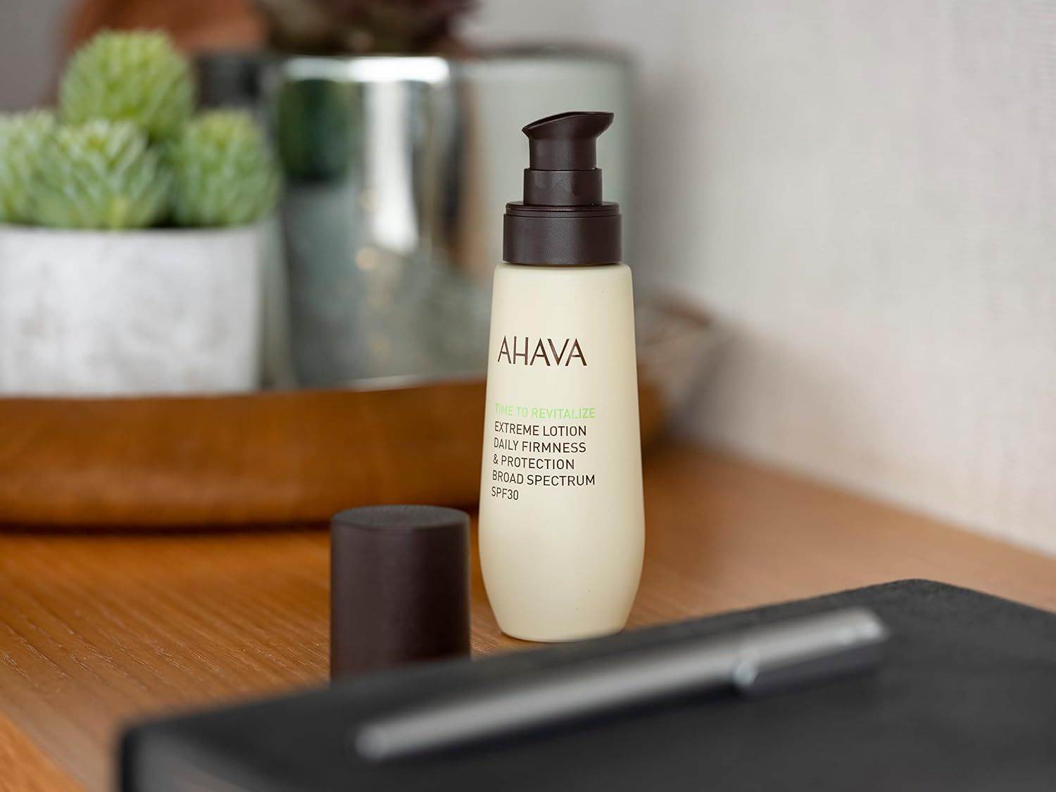 Ahava T.T.R. Extreme Lotion SPF30 auf einem Holztisch neben einem Notizbuch und Stift.