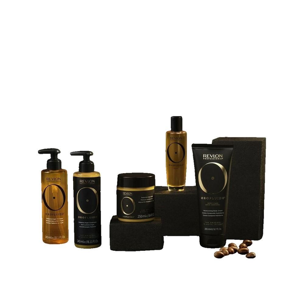 Orofluido-Produkte auf schwarzen Blöcken. Flaschen, Tiegel und Tube in Gold und Schwarz. Argan-Samen liegen daneben.