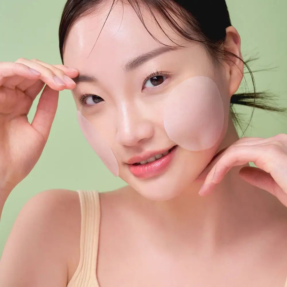 Frau mit Pads auf Wangen. Pads sind rund und transparent. Grüner Hintergrund.