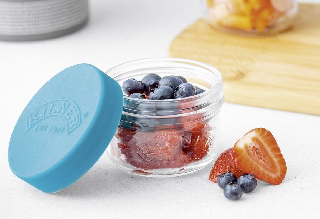 Glas mit blauem Deckel, gefüllt mit Erdbeeren. Daneben Erdbeeren und Blaubeeren. "KILNER" auf dem Glas.