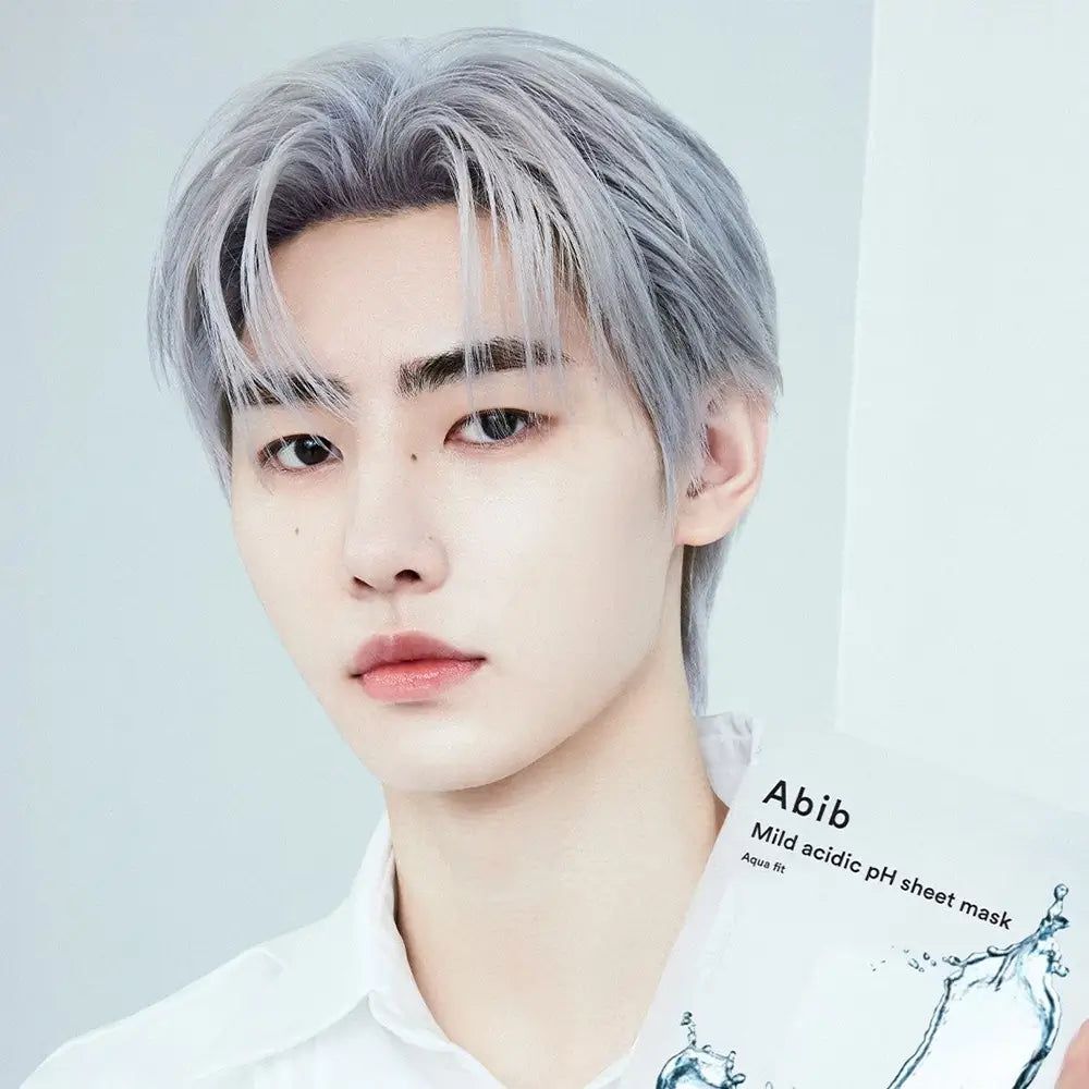 Person hält ABIB Milde Säure pH Gesichtsmaske Aqua Fit. Produktverpackung mit Produktnamen. Person mit grauen Haaren und hellem Hemd.